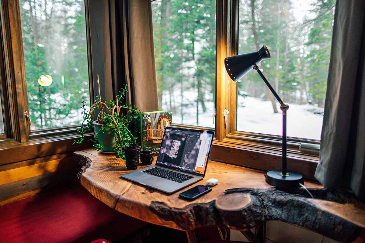 Un ordinateur portable sur un bureau en bois devant une fenêtre donnant sur la forêt